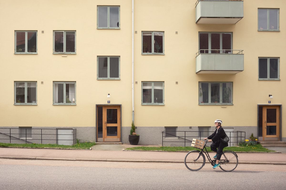 Foto av en kvinna som cyklar framför ett gult flerbostadshus.