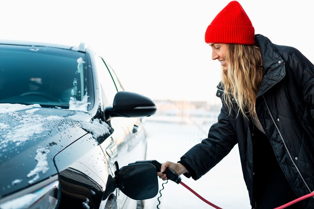 Foto av en kvinna som kopplar in laddaren i bilen utomhus i vinterväder