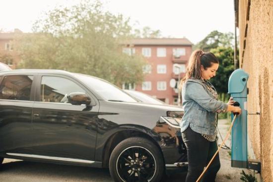 Foto av en kvinna som laddar elbil utanför sin bostadsrättsförening