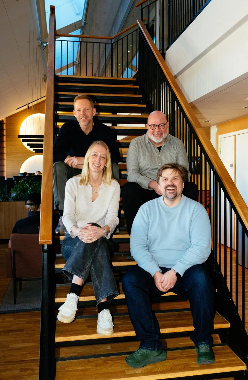 En kvinne og tre menn sitter i en trapp innendørs.