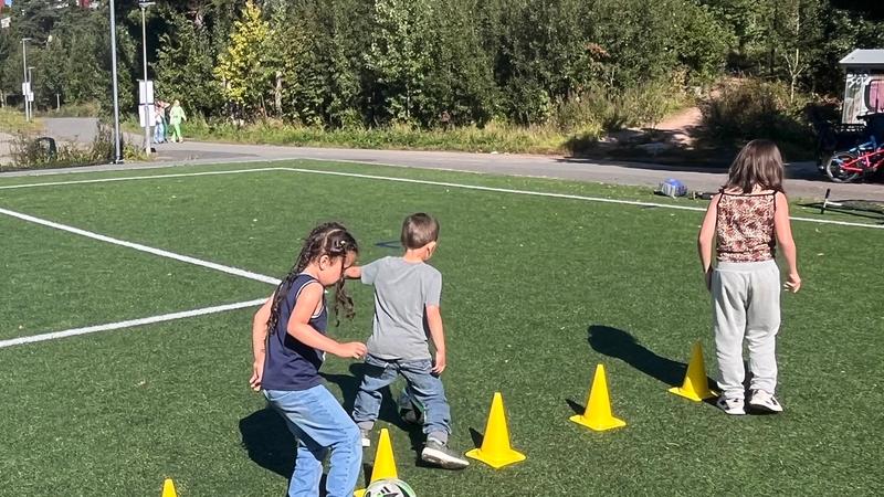 Tre barn sparker fotball i slalom mellom kjegler.