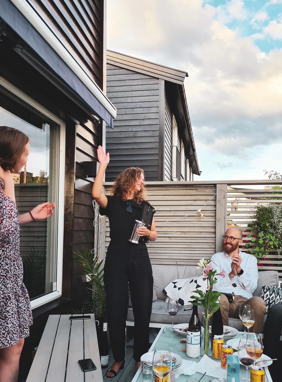 En gjeng mennesker pÄ en terrasse, Ragne holder en pokal.
