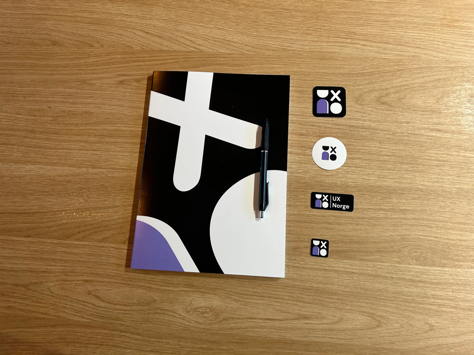 UX Norge-skisseblokk, penn og klistremerker ligger på et bord.