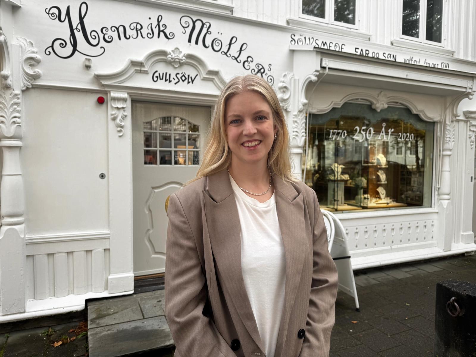 Portrett av smilende kvinne foran en klassisk hvit butikkfasade for Henrik Møllers Gullsølv.