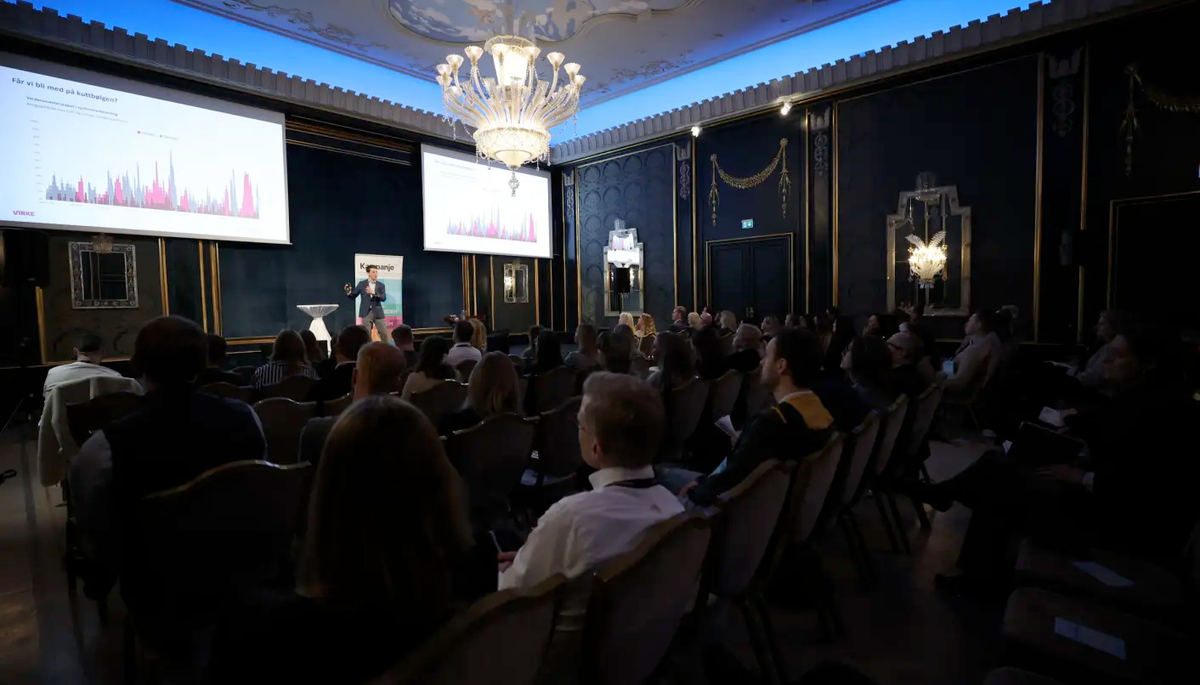 Mennesker sitter i mørk sal med presentasjon på scenen.