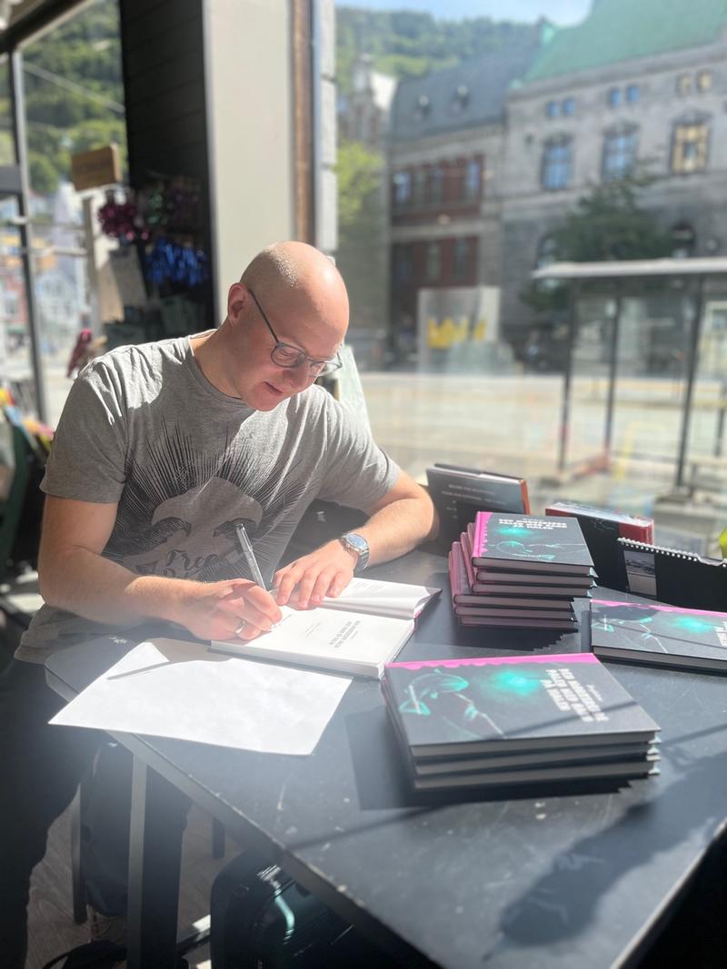 Mann sitter i butikkvindu og singerer bøker