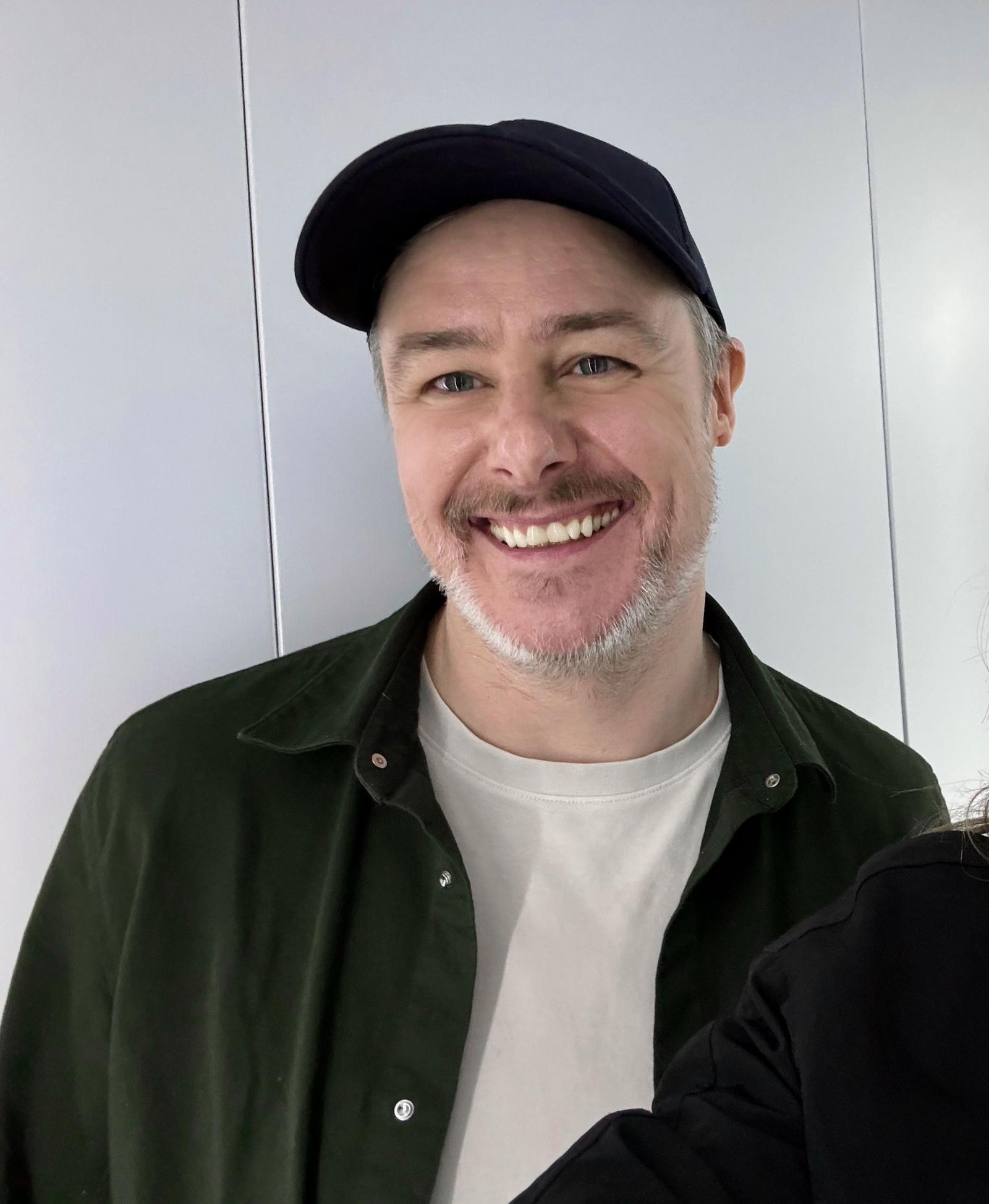 Smilende mann med svart caps og grønn skjorte.