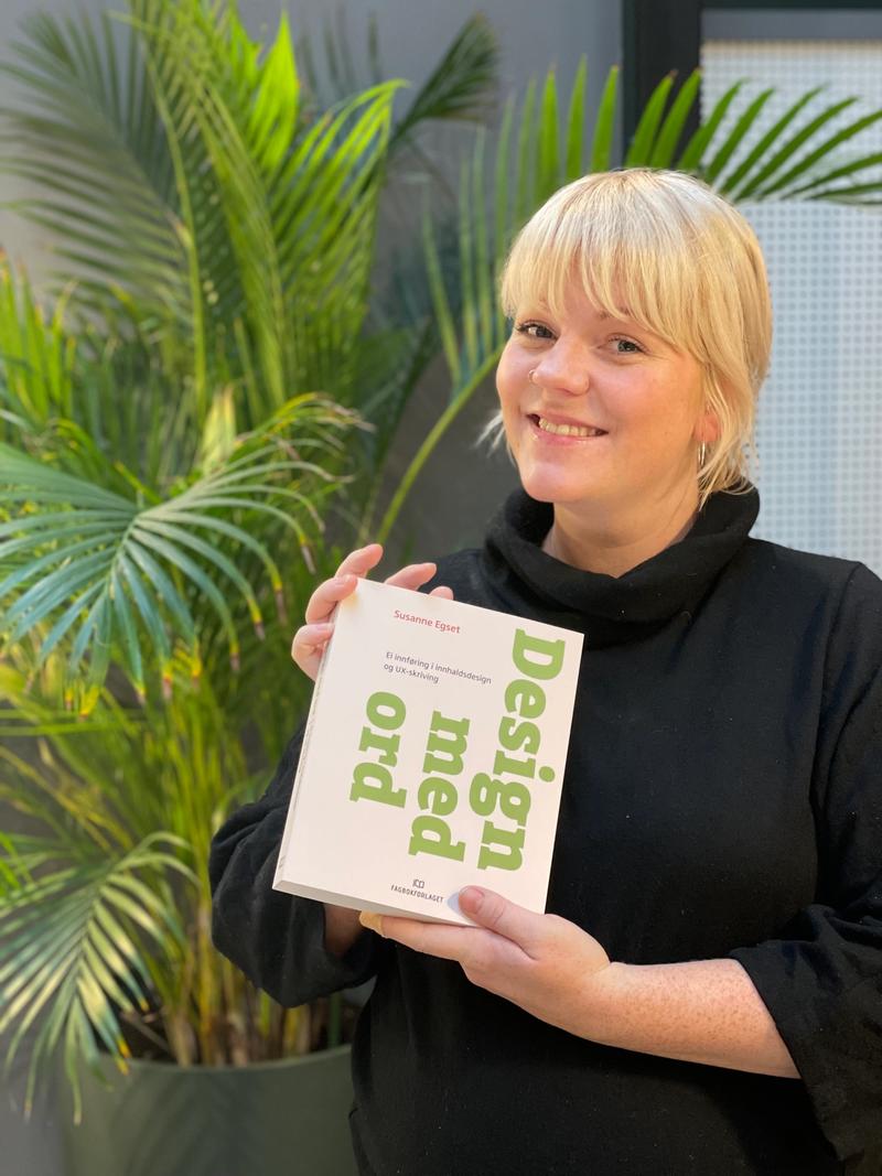 Kvinne smiler og holder frem boken "Design med ord".