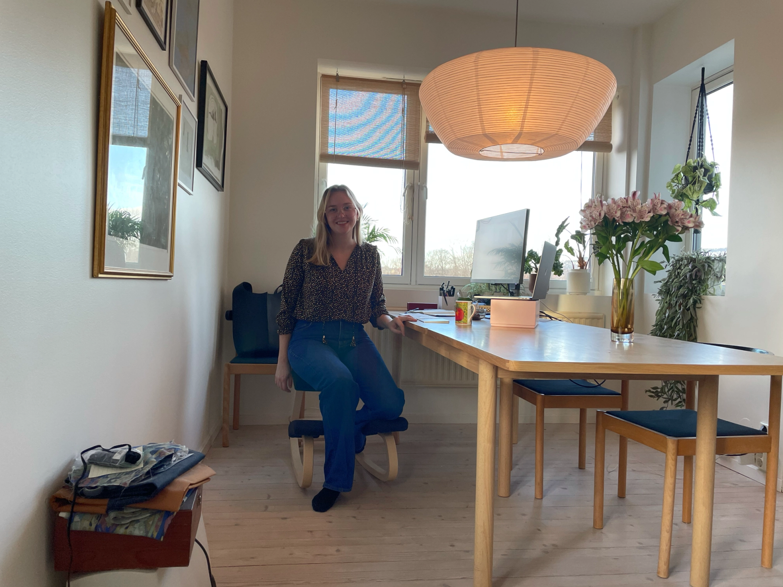 Dame sitter med spisebord, hvor det er opprettet arbeidsstasjon med PC-skjerm og laptop.