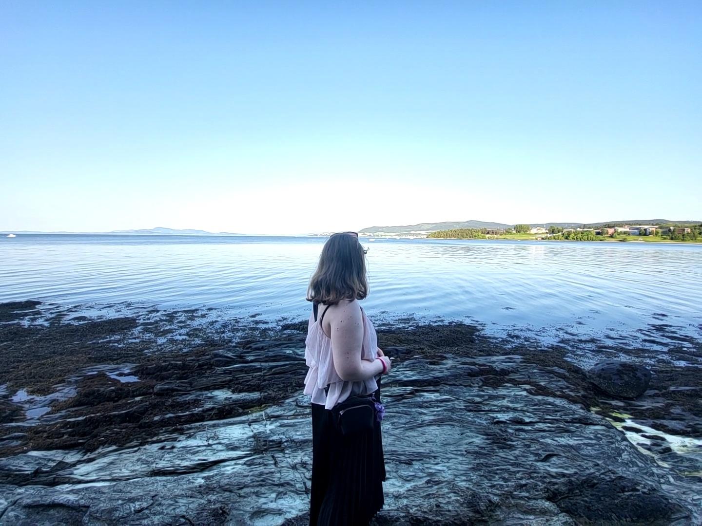 En dame står i fjæra.