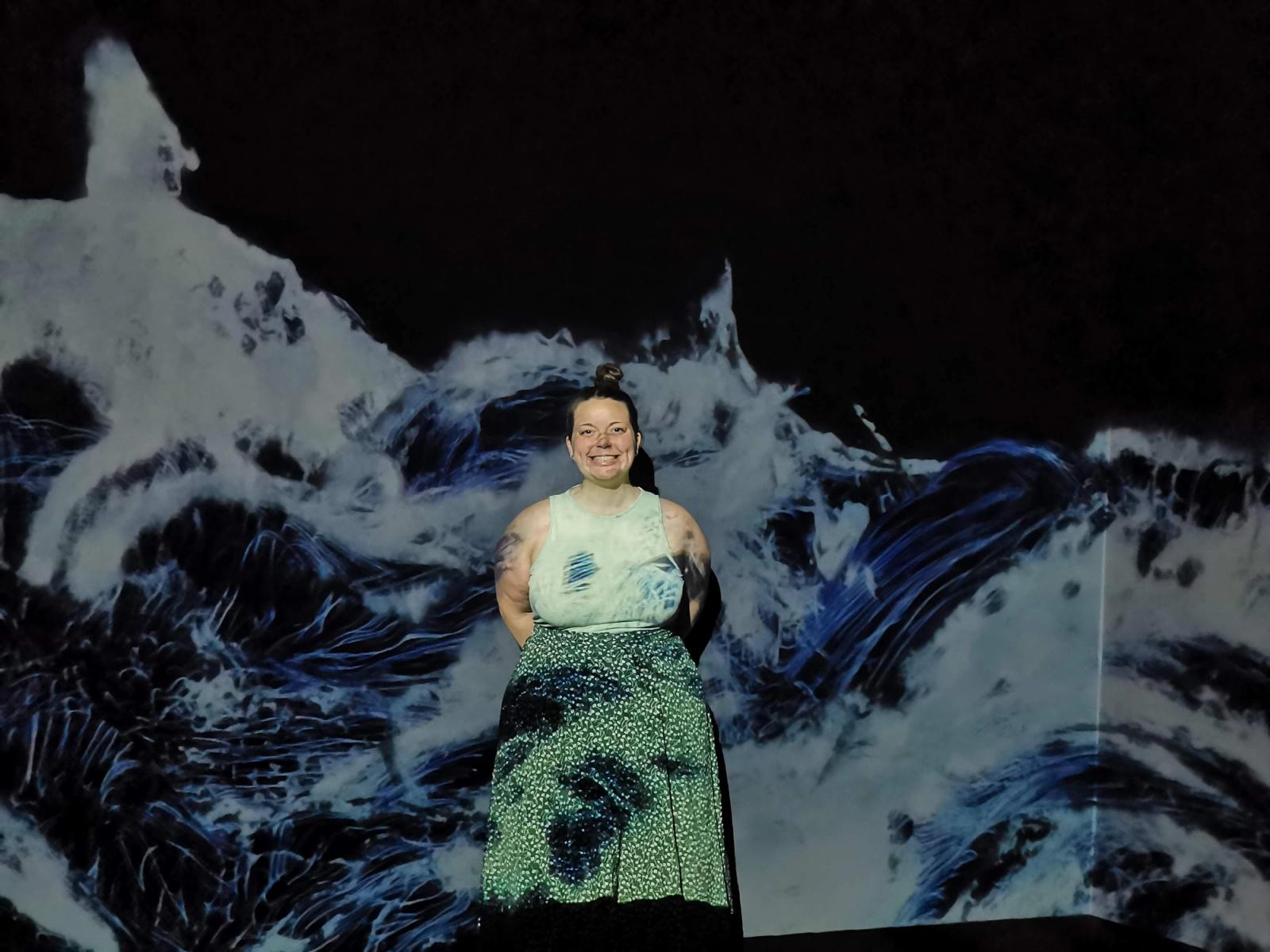 Dame står inntil vegg hvor lysprojektor projekterer bilder av havet over henne.