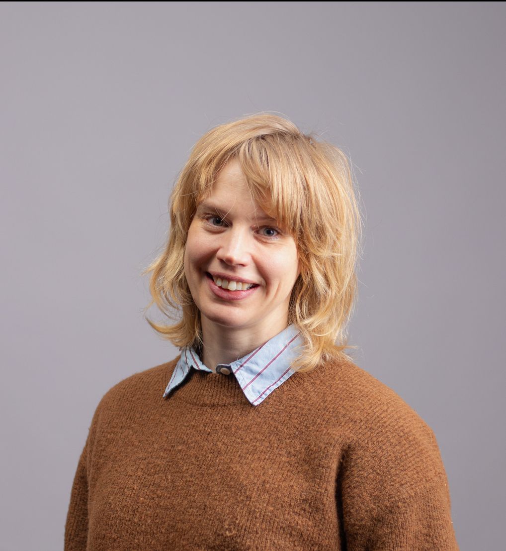 Profesjonelt portrett av smilende dame med skjorte og genser og langt lyst hår. 