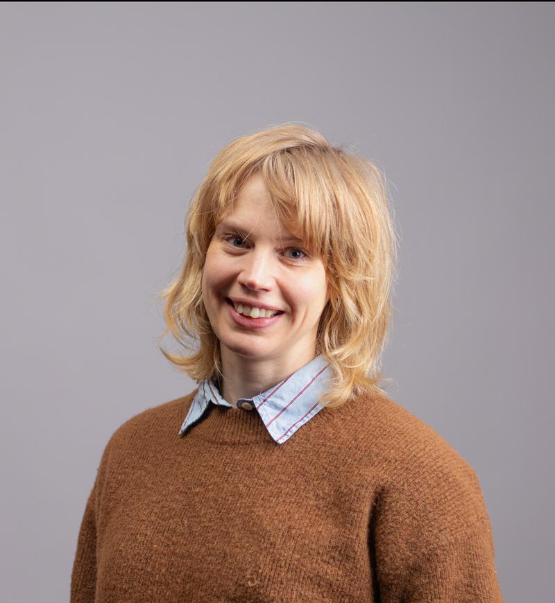 Profesjonelt portrett av smilende dame med skjorte og genser og langt lyst hår.