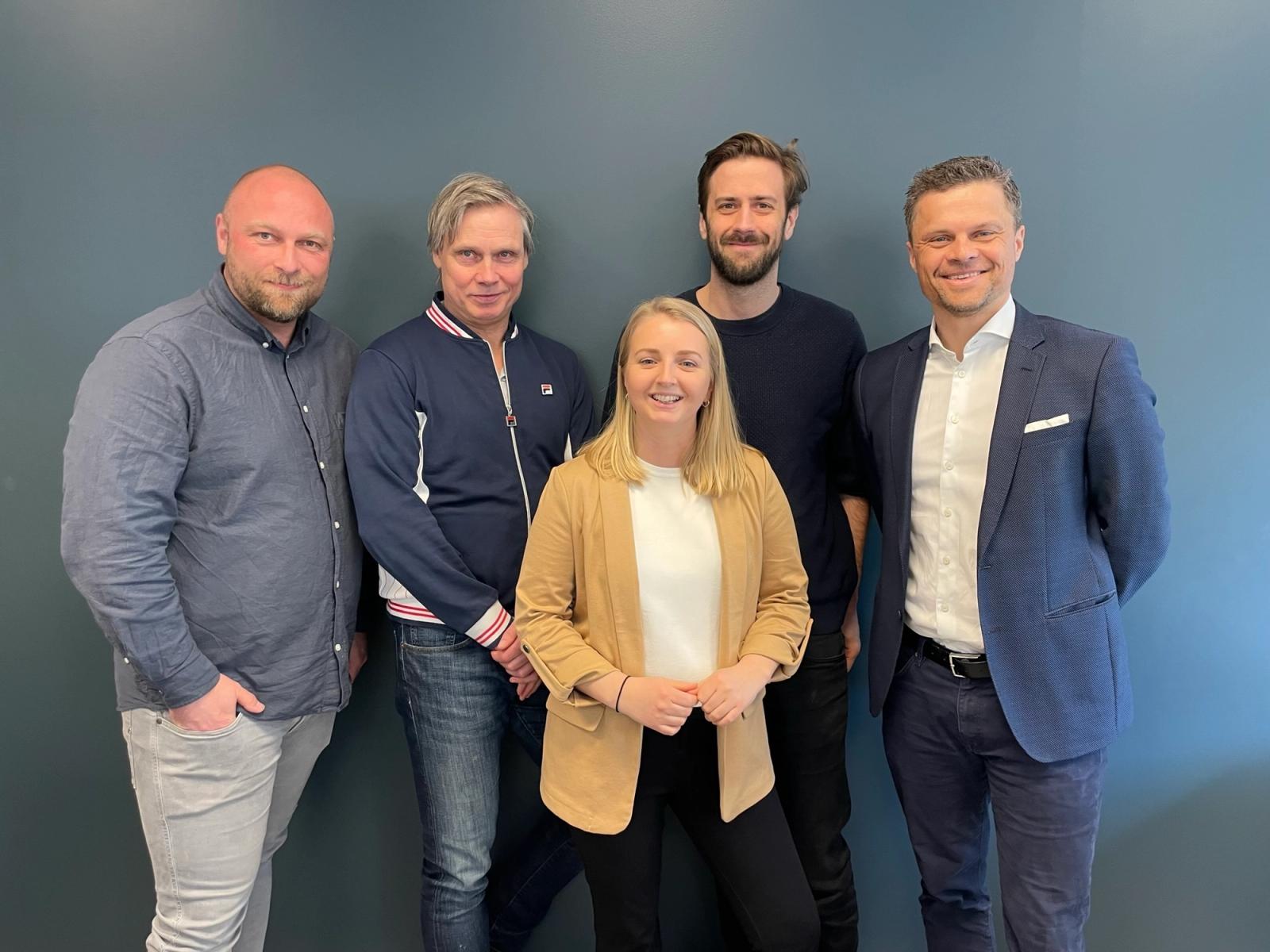 Fire menn og ei dame smiler til kamera