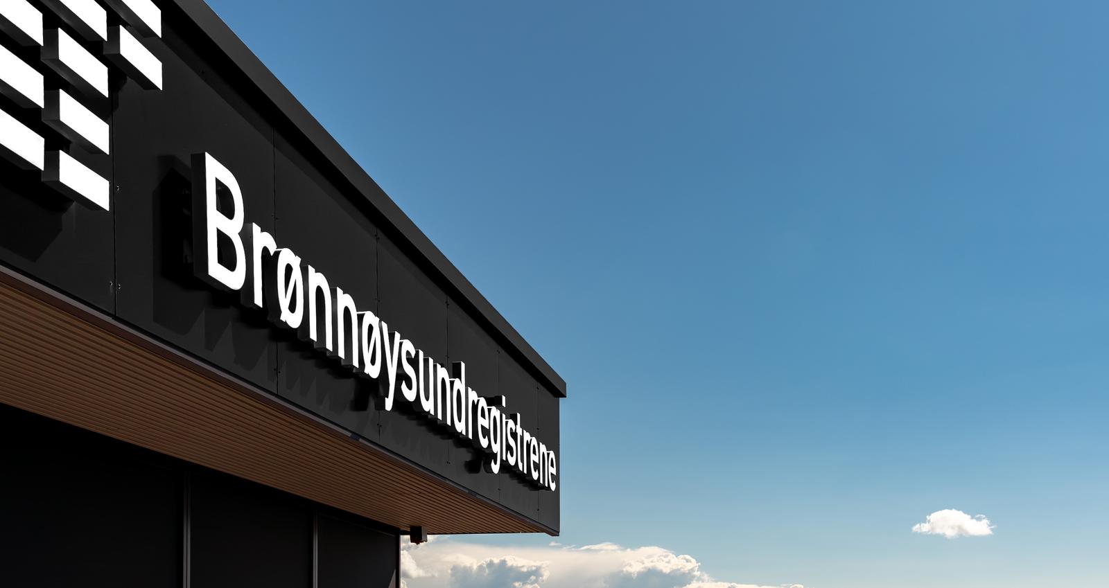 Hovedkontoret til Brønnøysundregistrene, sett utenfra. I bakgrunnen vakkert kystlandskap og blå himmel.