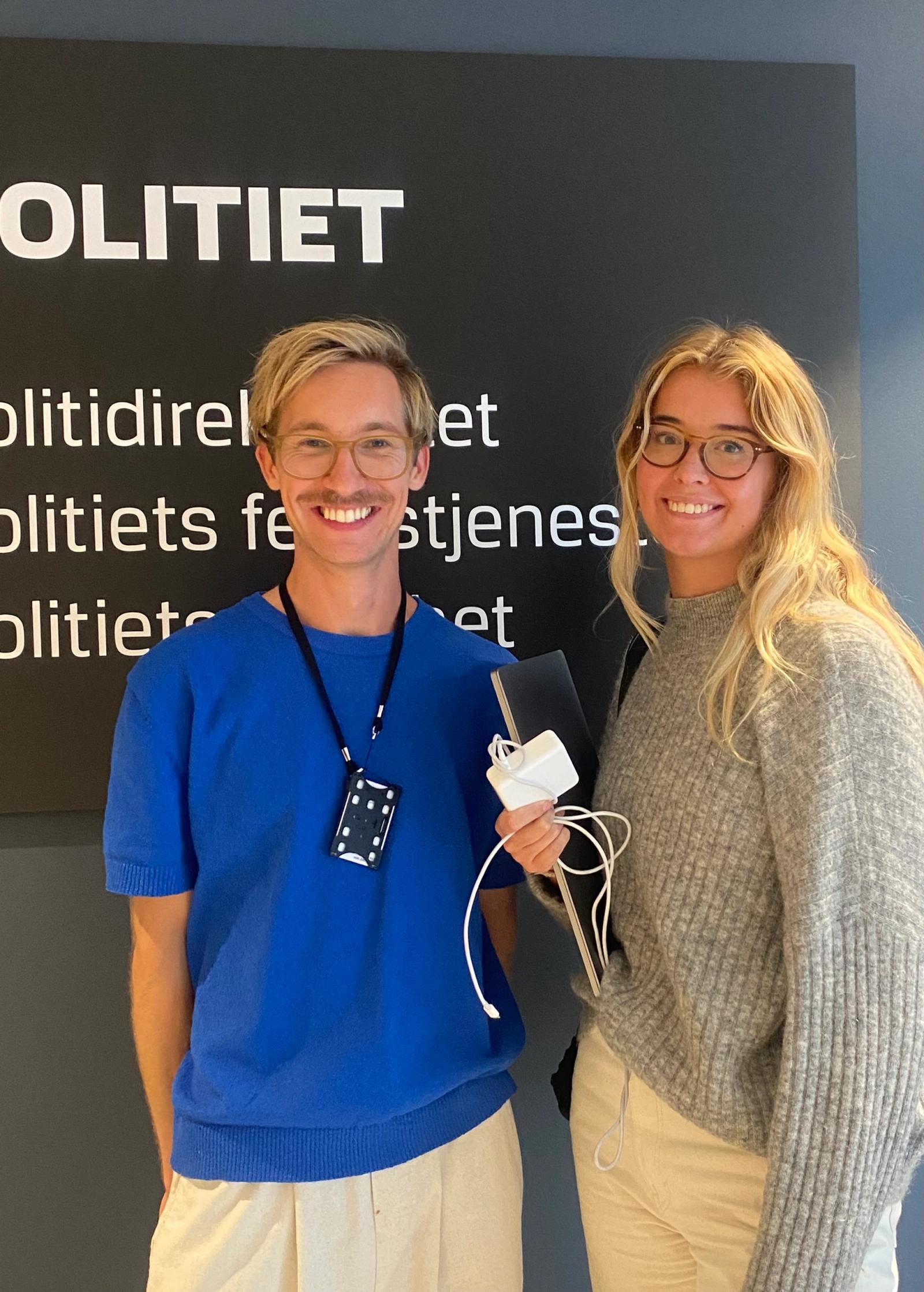 En mann og en kvinne smiler foran politiets logo