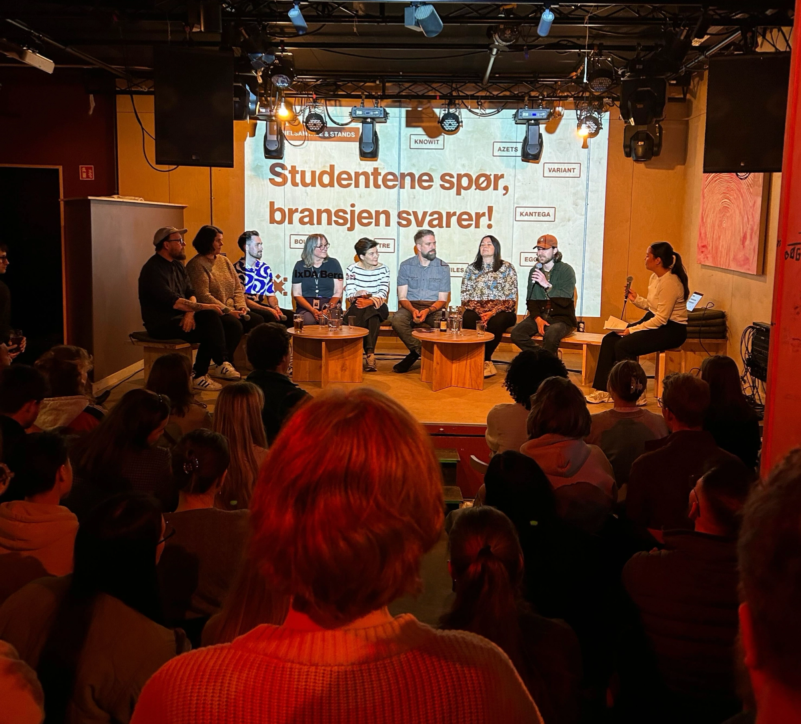 Mennesker sitter på en scene, publikum i mørket foran.