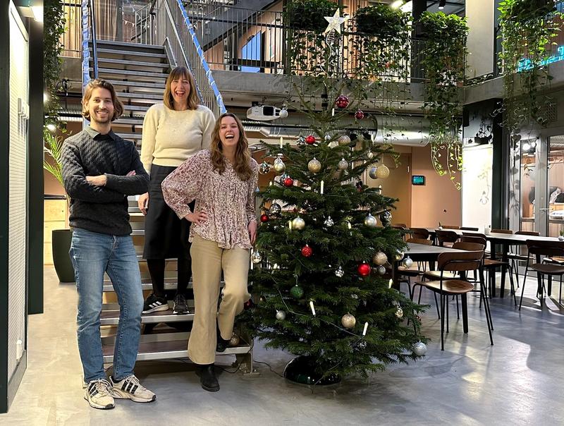 De tre nyansatte står i en trapp ved et pyntet juletre.