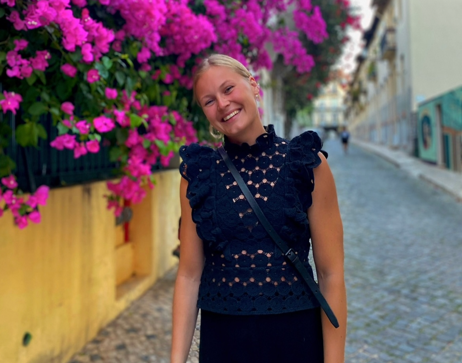 Dame med blåndt hår i hestehale står framfor knæsj rosa blomster.