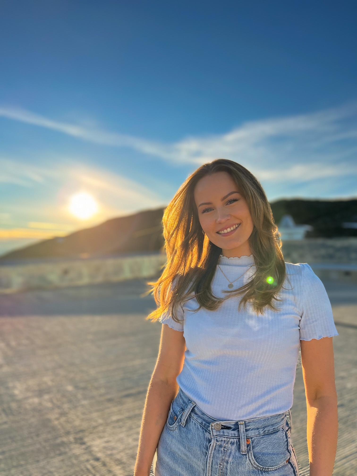 Dame står utendørs med solen i bakgrunnen. Solen gir henne en fin glød i det lange håret.