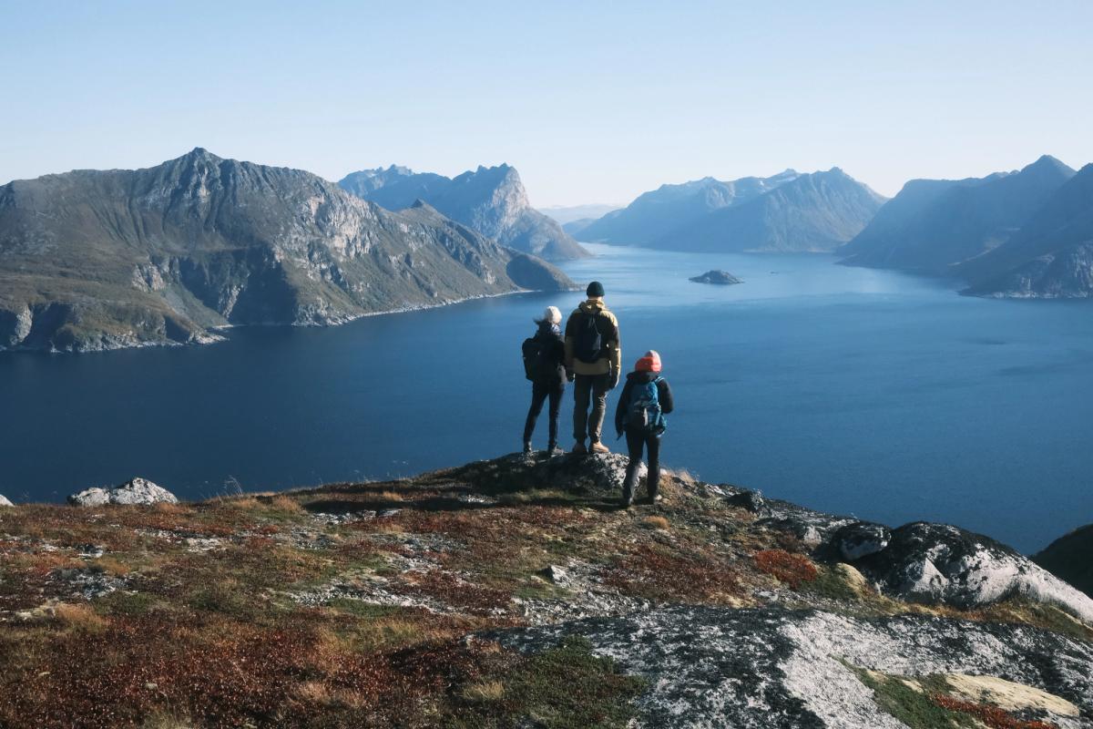 Tre personer stÄr pÄ en fjelltopp og ser utover havet.