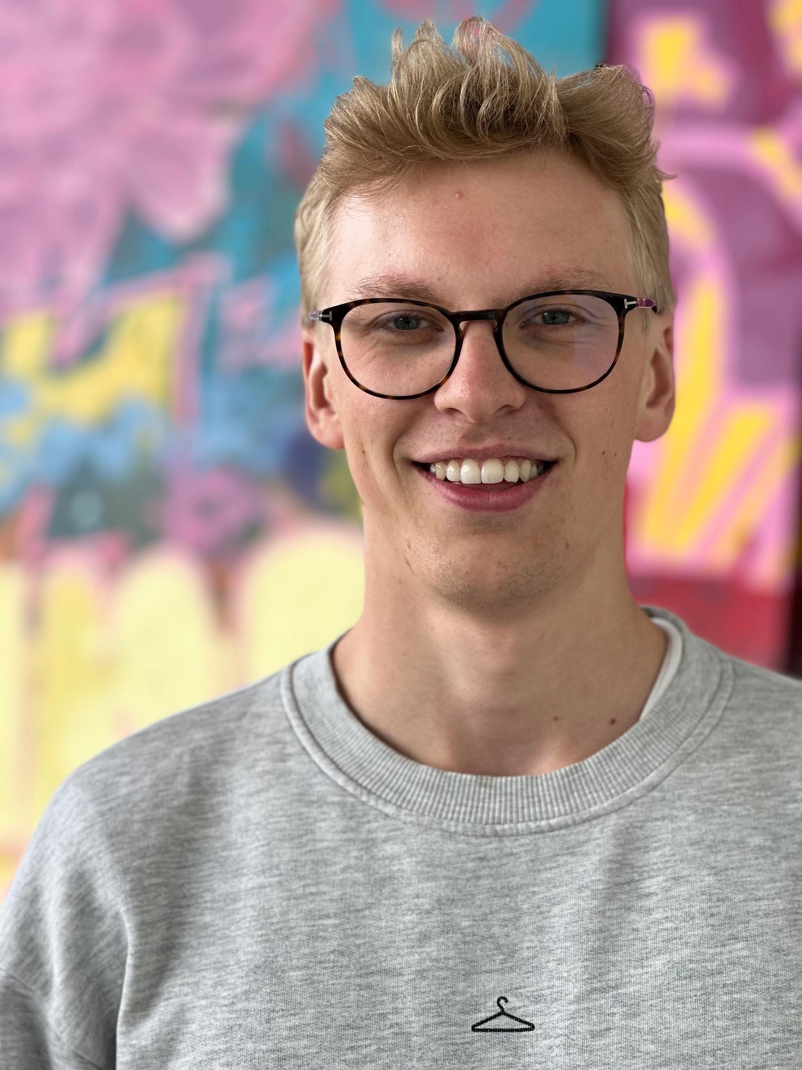 Blond mann med svarte briller og grå crew-neck genser.