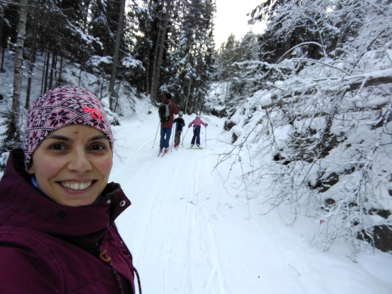 Dame tar selfie i snølandskap, hvor mann og to barn er i bakgrunnen på ski.