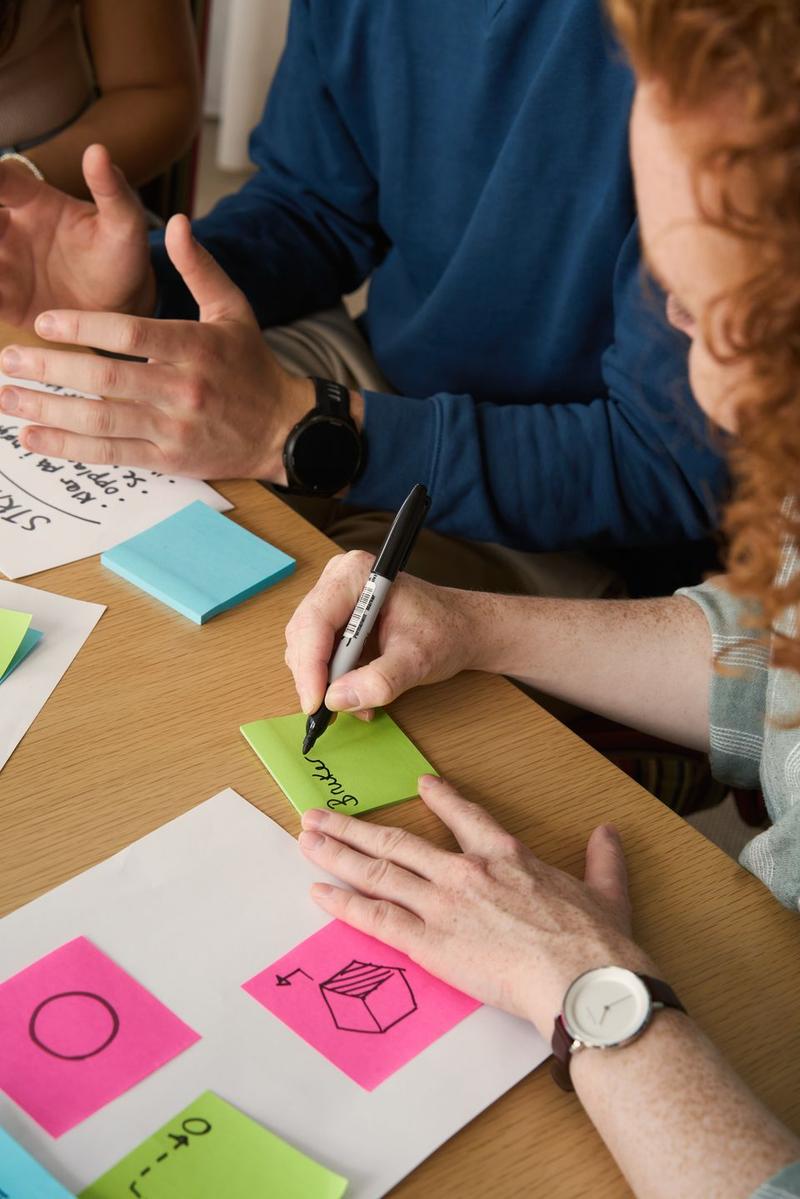 Mennesker sitter ved et bord og skriver og tegner på Post-it-lapper