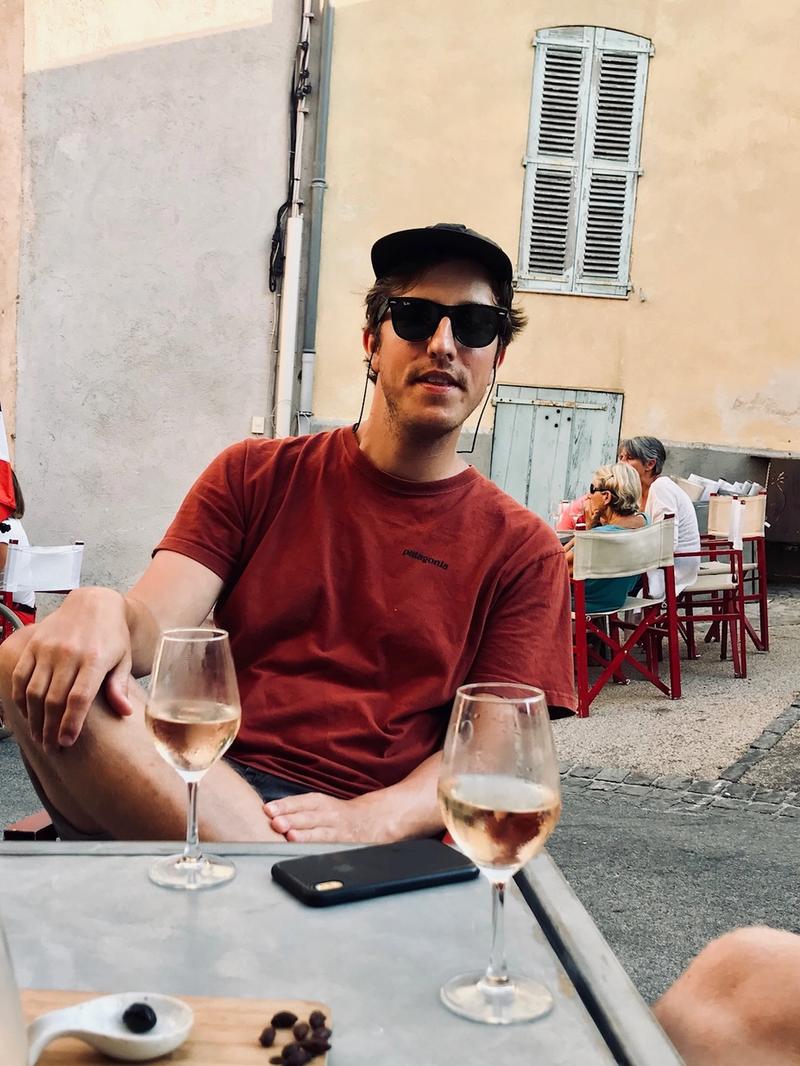 Mann med solbriller og caps sitter utendørs i bakhage og drikker rosévin og spiser på oliven.