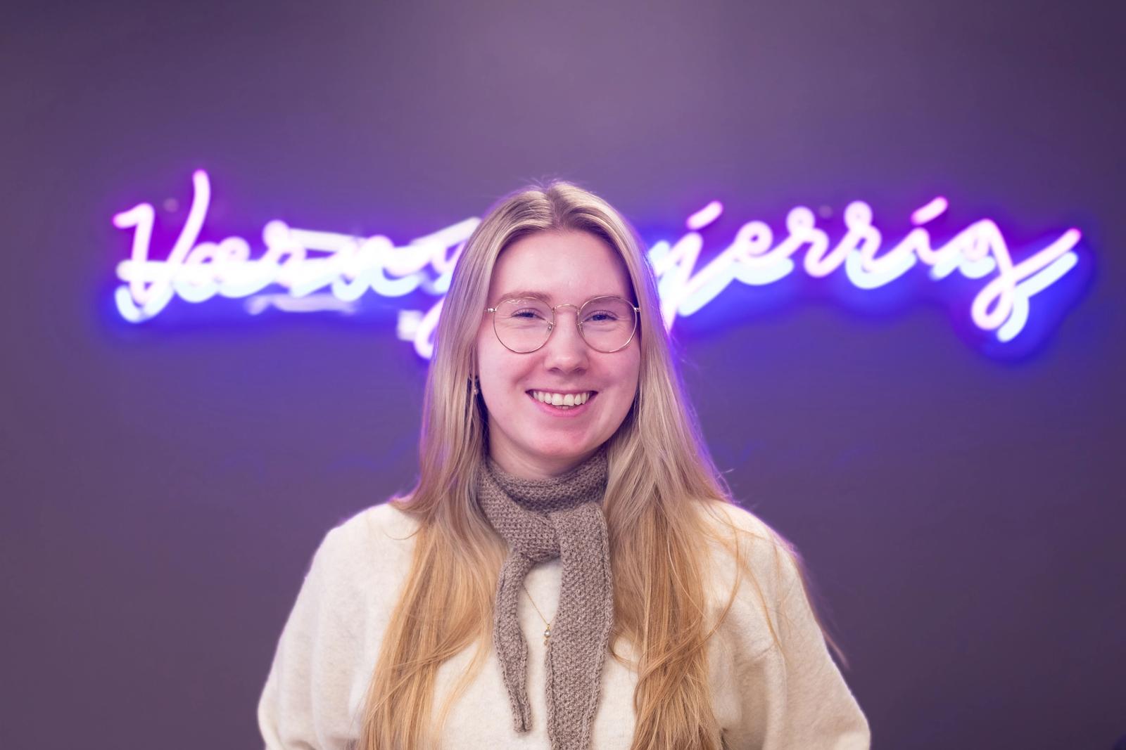 Dame med lyst, langt hår og biller med neon-skilt i bakgrunnen.