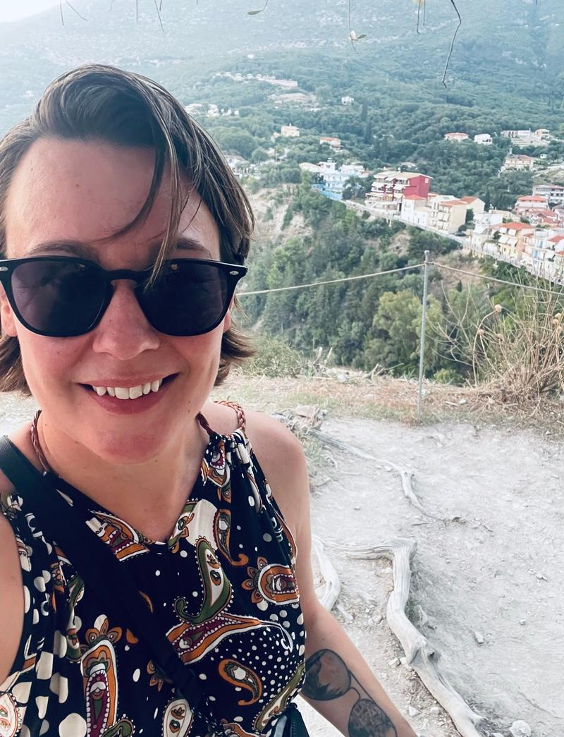 Selfie av Saja fra en fjelltopp med hus i bakgrunnen. Hun har på seg solbriller og en kjole med et grafisk mønster.