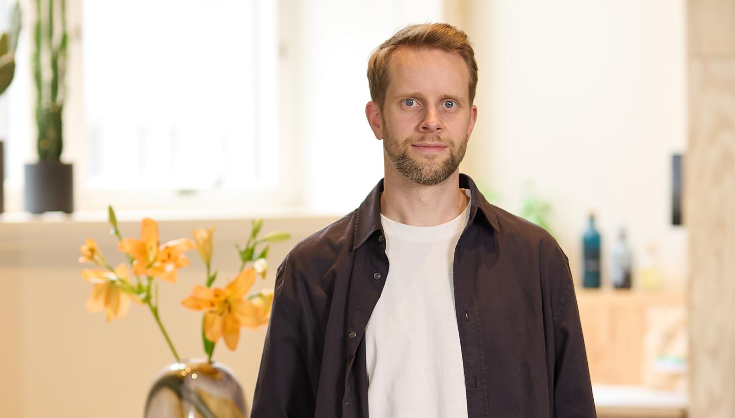 Portrettbilde av mann med kort skjegg og blå øyne i kontorlanskap.