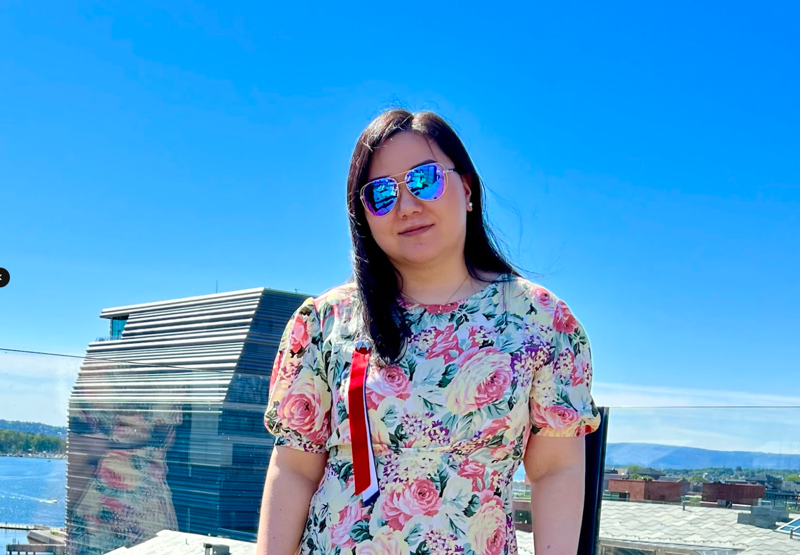 Dame med blomster-t-skjorte, 17-mai sløyfe og solbriller står på toppen av opera-taket i sommervær.