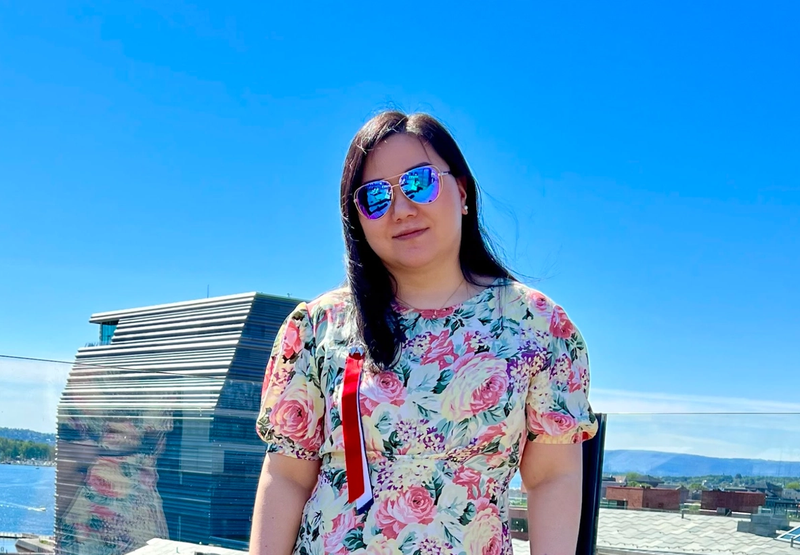 Dame med blomster-t-skjorte, 17-mai sløyfe og solbriller står på toppen av opera-taket i sommervær.