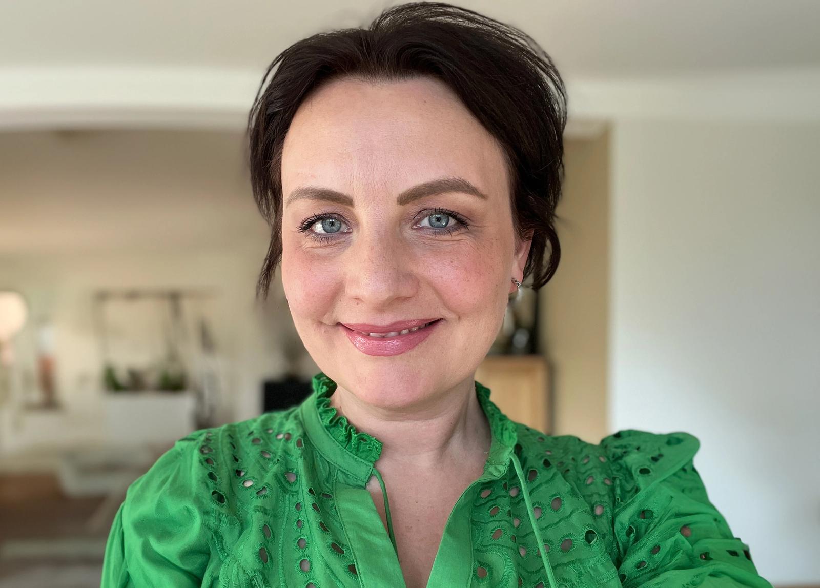 Et portrettbilde av Ingvill Helen Kjørlaug. Hun har på seg en grønn skjorte, har blå øyne og svart hår som er satt opp.