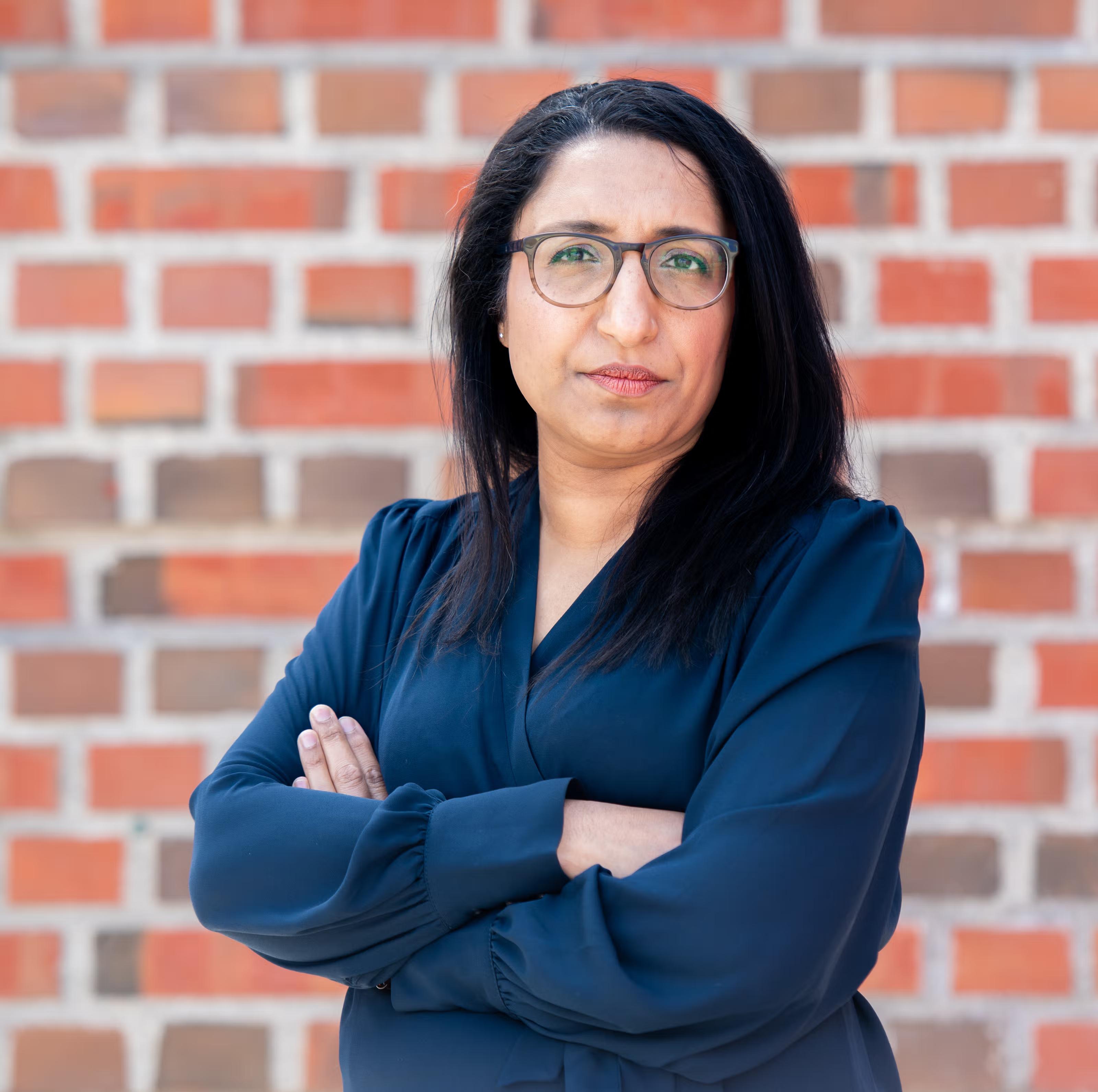 Kvinne med mørkt hår, briller og mørk blå bluse.