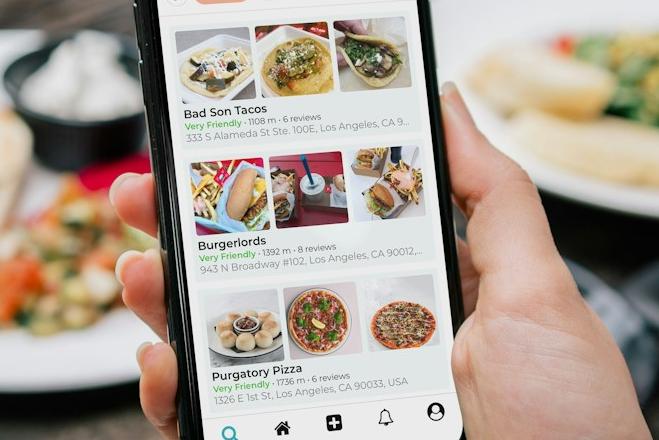 En person holder en telefon med en matbestilling-app opp foran et bord med forskjellige matretter på.