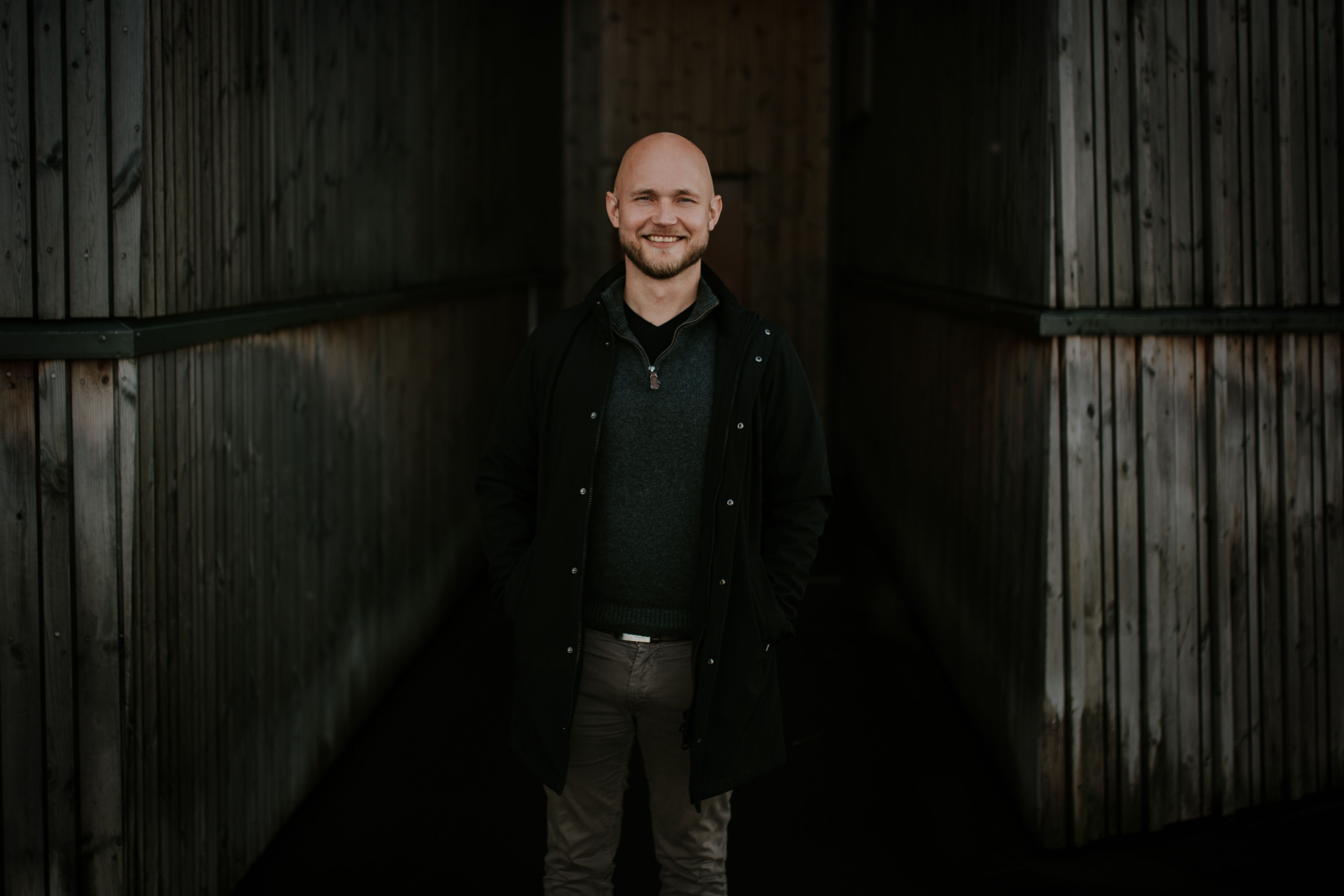 Erling står med en mørk bakgrunn, i en frakk og smiler