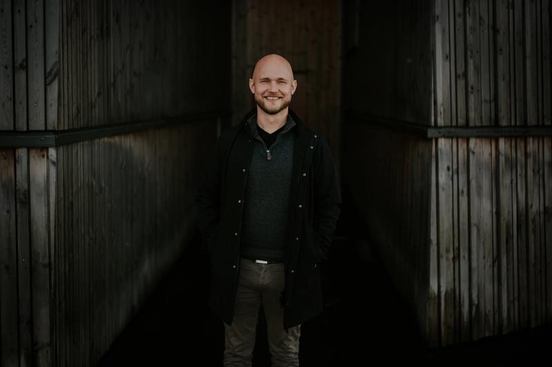 Erling står med en mørk bakgrunn, i en frakk og smiler