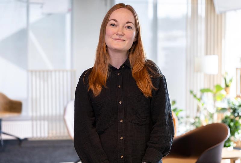 Dame i kontorlandskap med svart skjorte og langt rødt hår med midtskille.