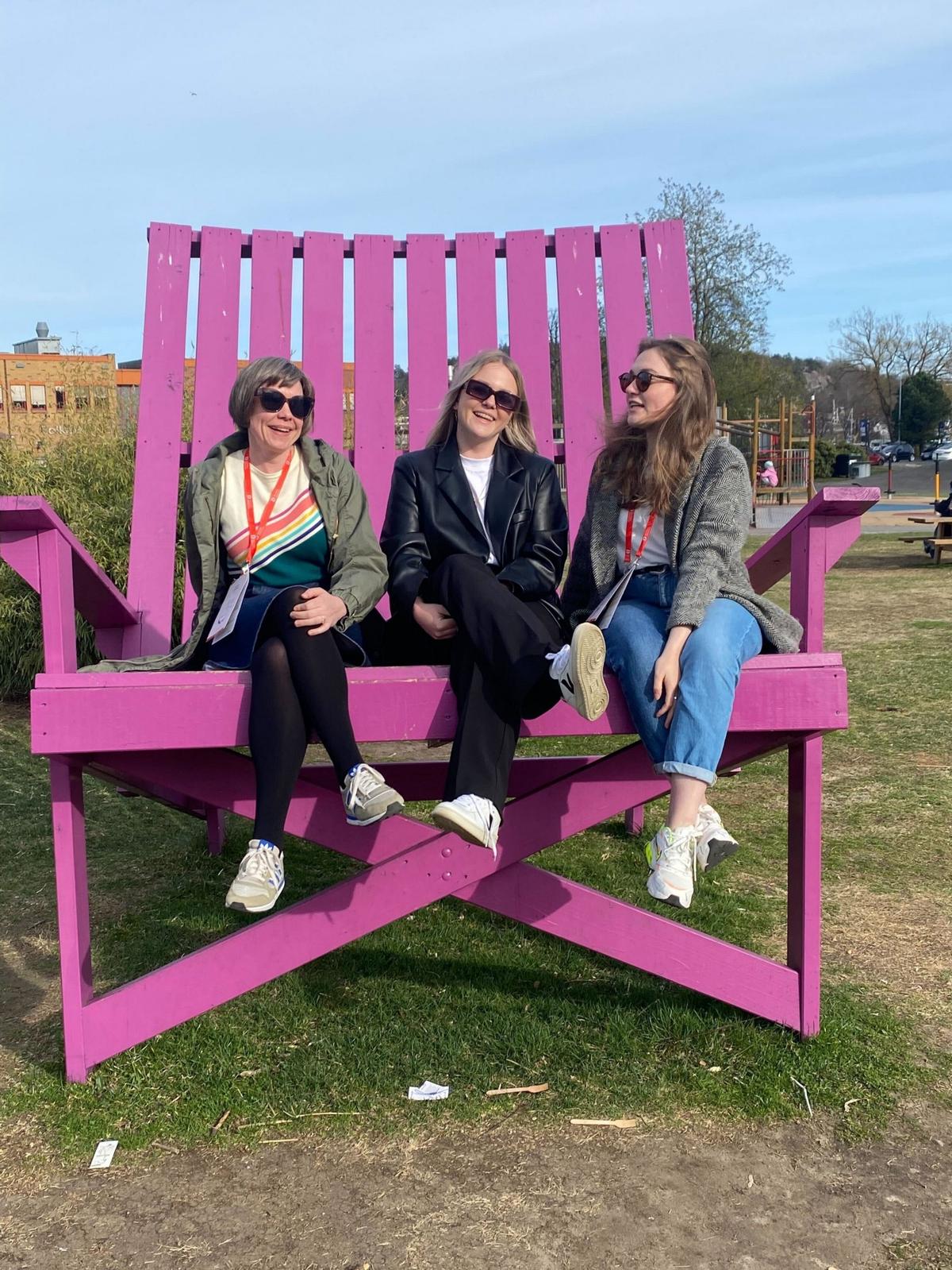 Tre damer i en veldig stor, rosa stol på en plen