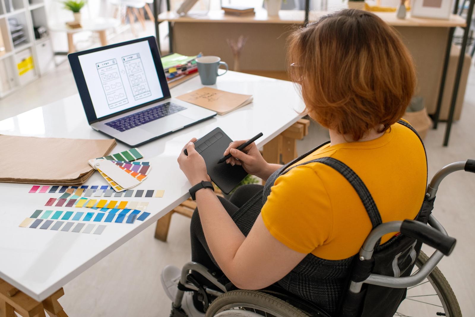 Dame i rullestol foran en laptop med trådskisser på skjermen.