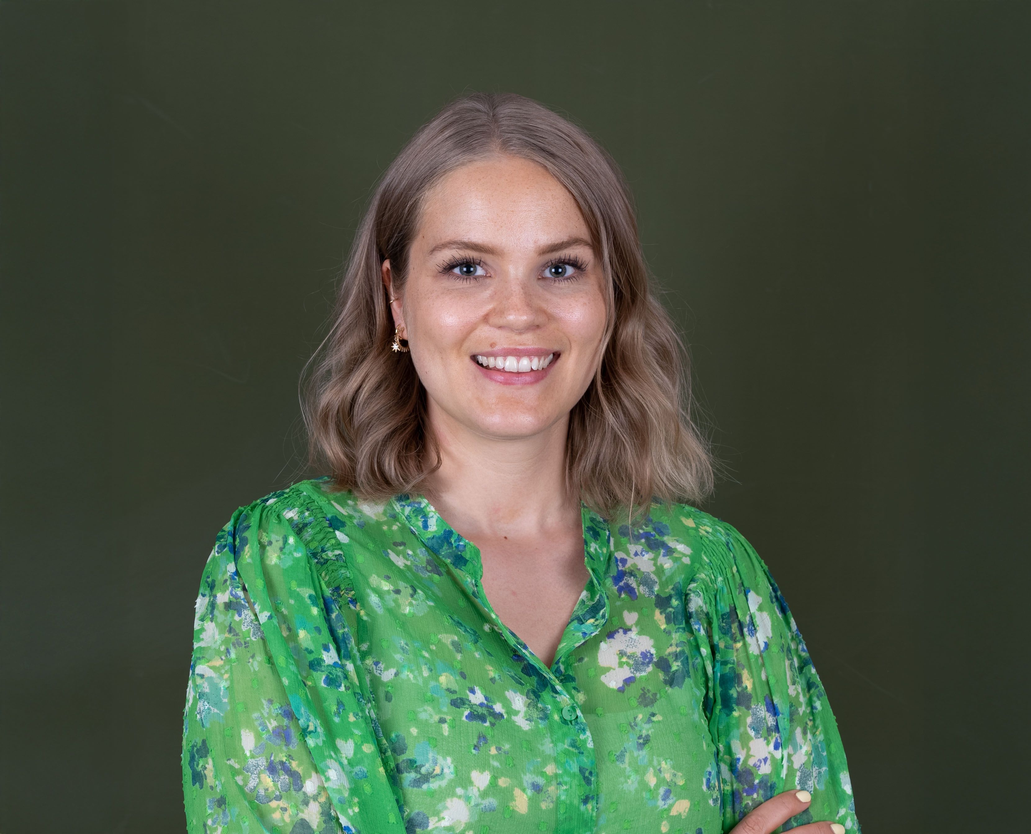 Portrettbilde av dame med nøtteblondt hår til skuldrene og grønn kjole med blomster på. 