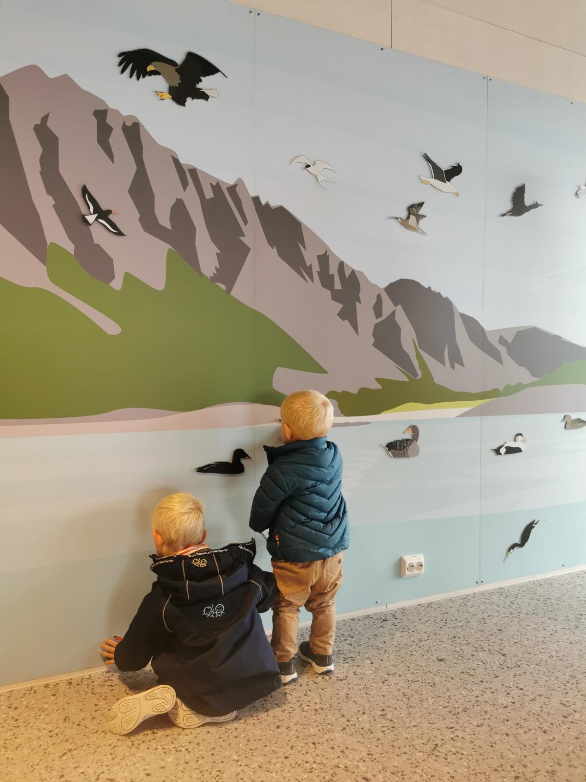 To små gutter slytter på magneter som ligner fugler og fisk på en malt vegg med sjø og fjell.