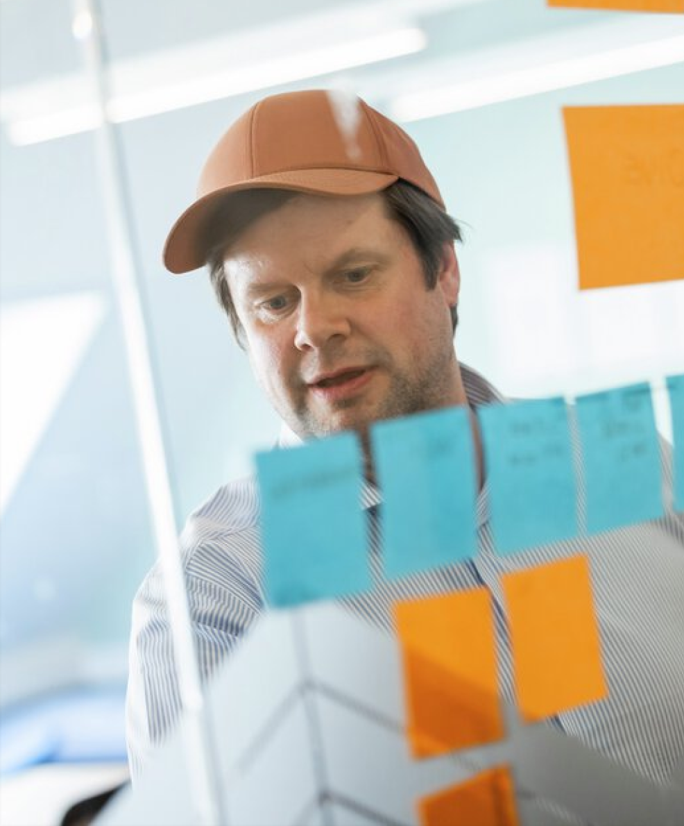Mann i caps står foran en glassvegg med post-it-lapper i forskjellige farger.