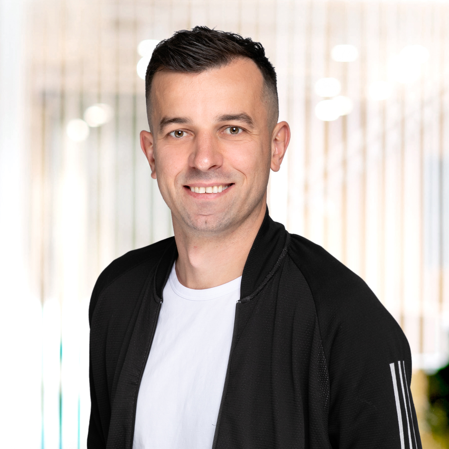 Mann med mørkt hår, svart jakke og hvit t-skjorte