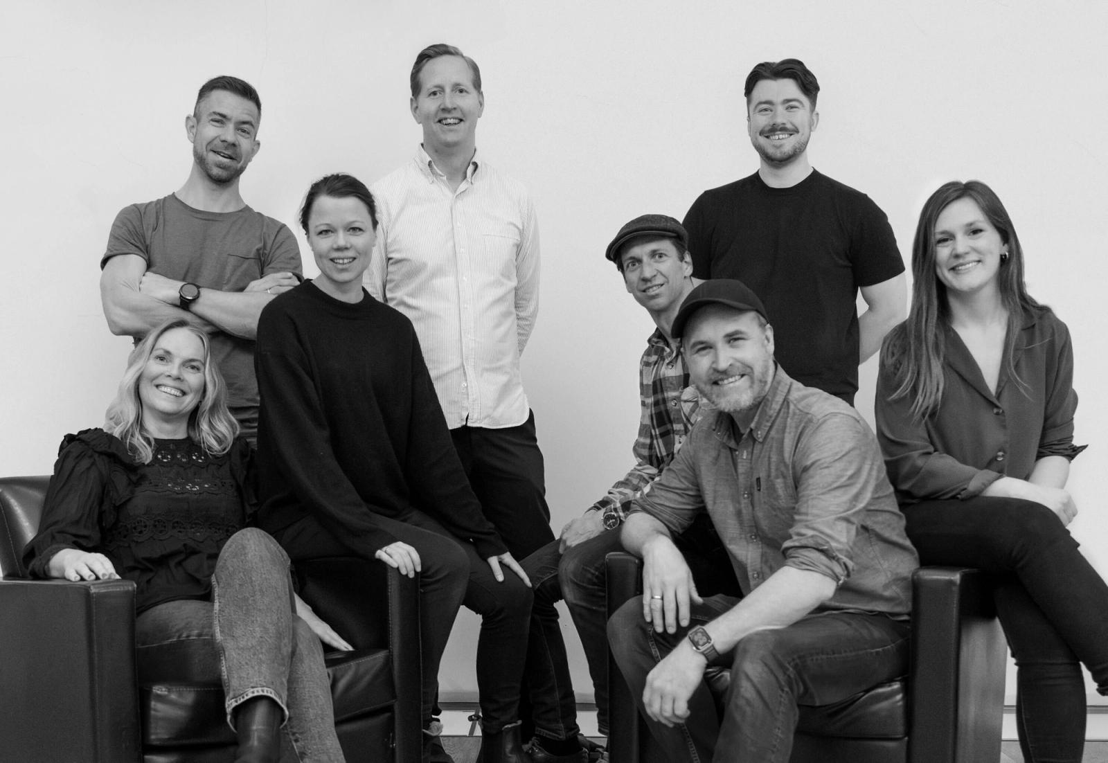 Åtte mennesker står og sitter på et svart/hvitt-bilde
