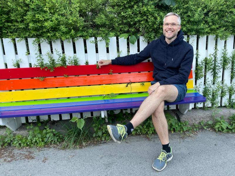 Jon Olav H. Eikenes sitter på en regnbuefarget benk.