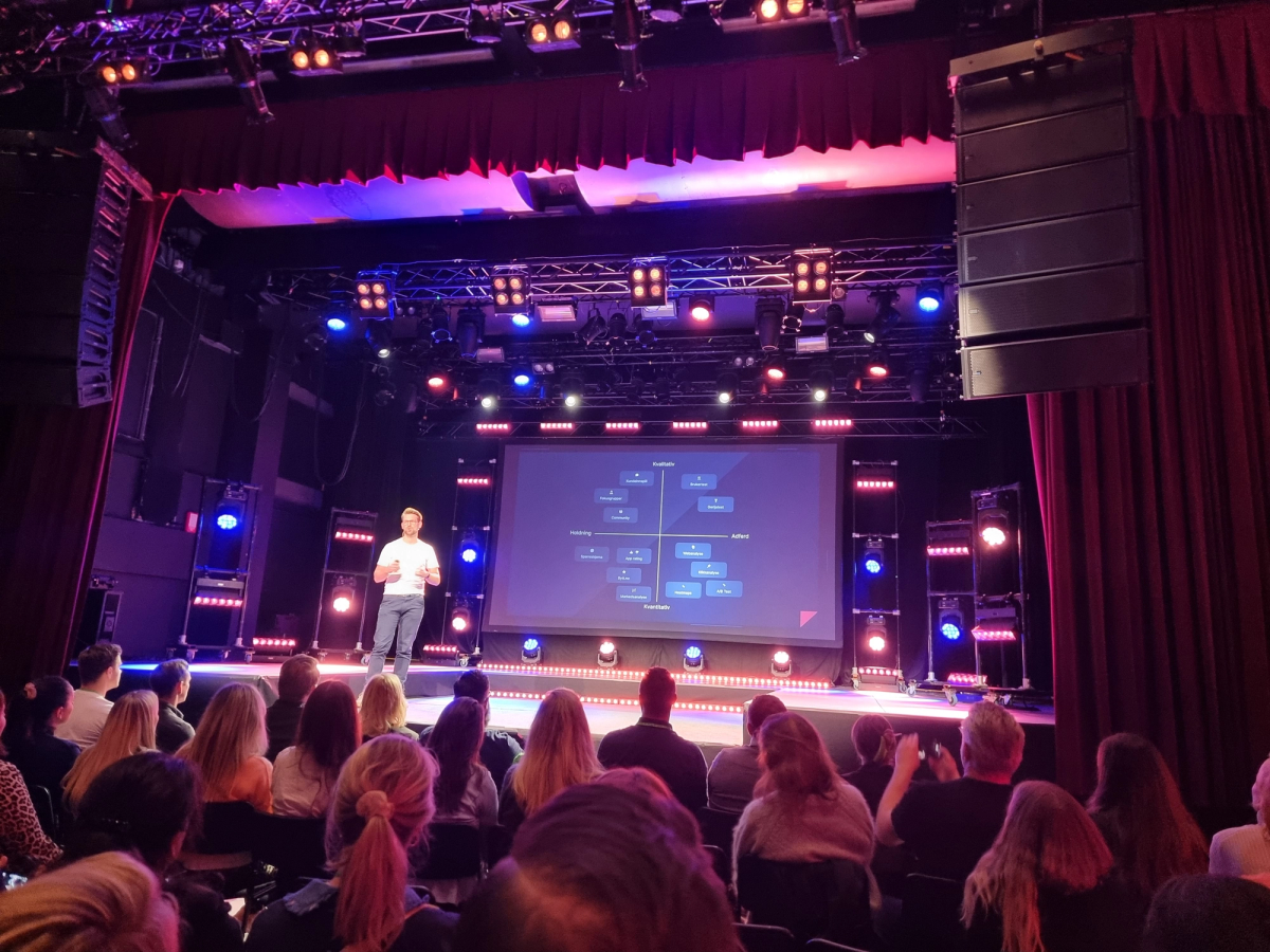 En mann står på scenen foran publikum. Foto