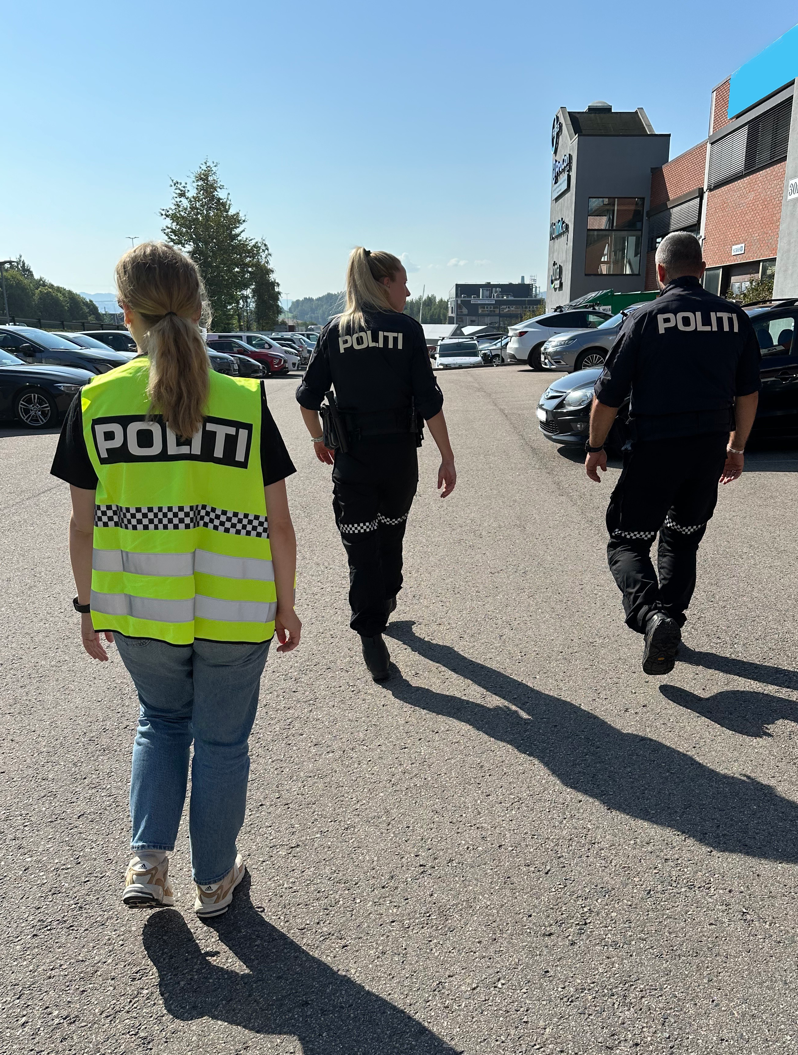 Tre personer går ute, to i politiuniform og den tredje med gul vest som det står Politi på.